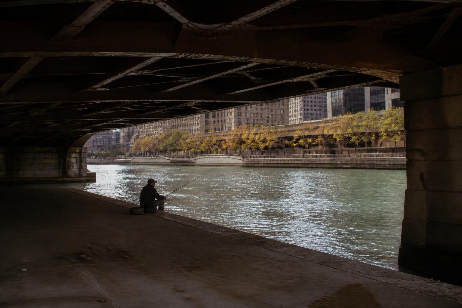 A man fishing under a steel city bridge