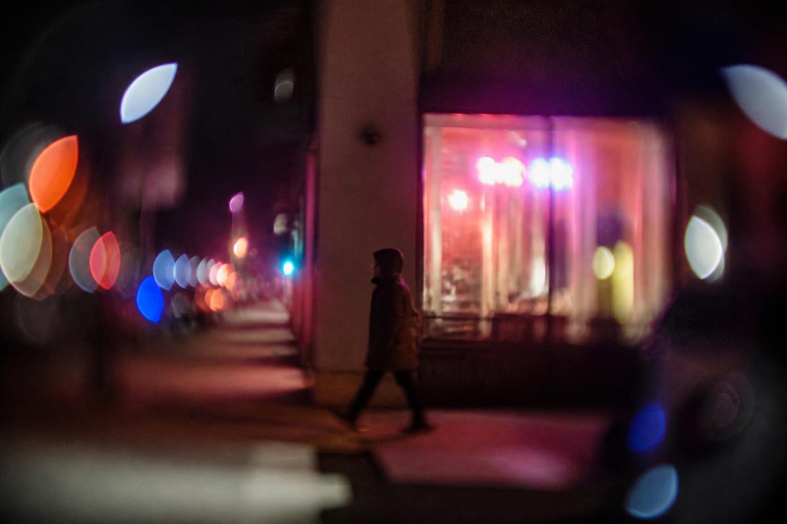 Night street with swirly neon bokeh behind a pedestrian